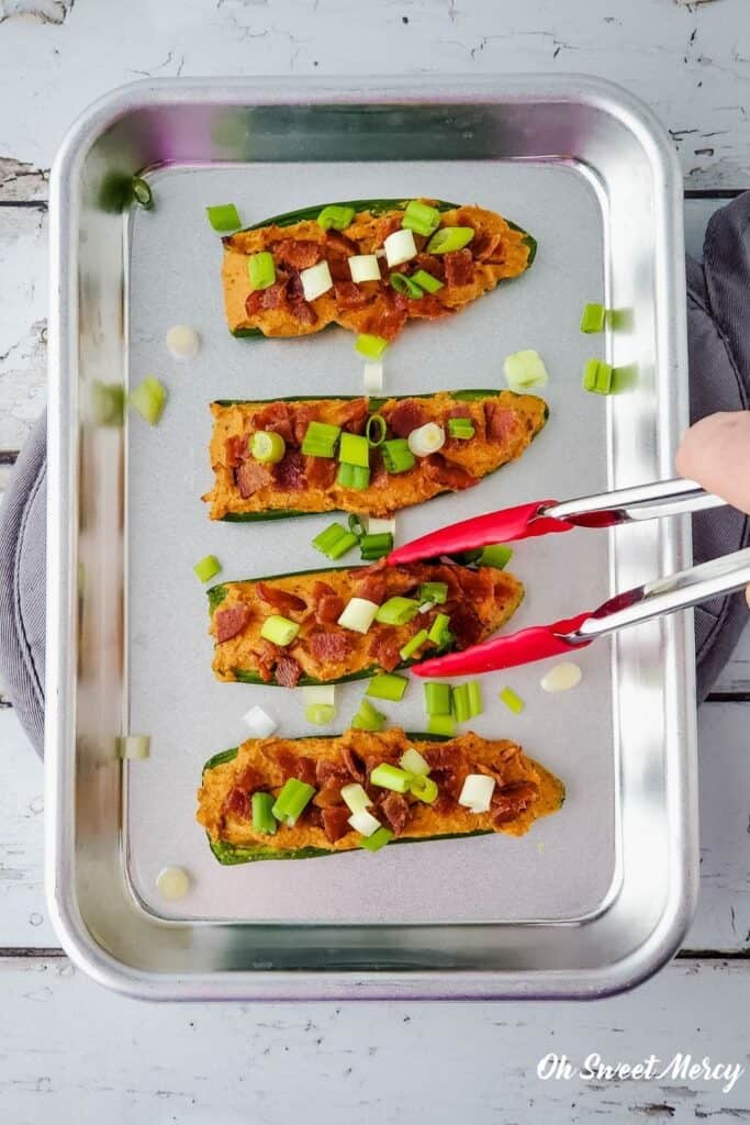 4 jalapeno popper halves on a tray, using tongs to pick one up