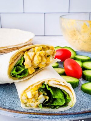 Creamy Ranch Egg Salad Wrap cut in half, on a plate with cucumber slices and cherry tomatoes.