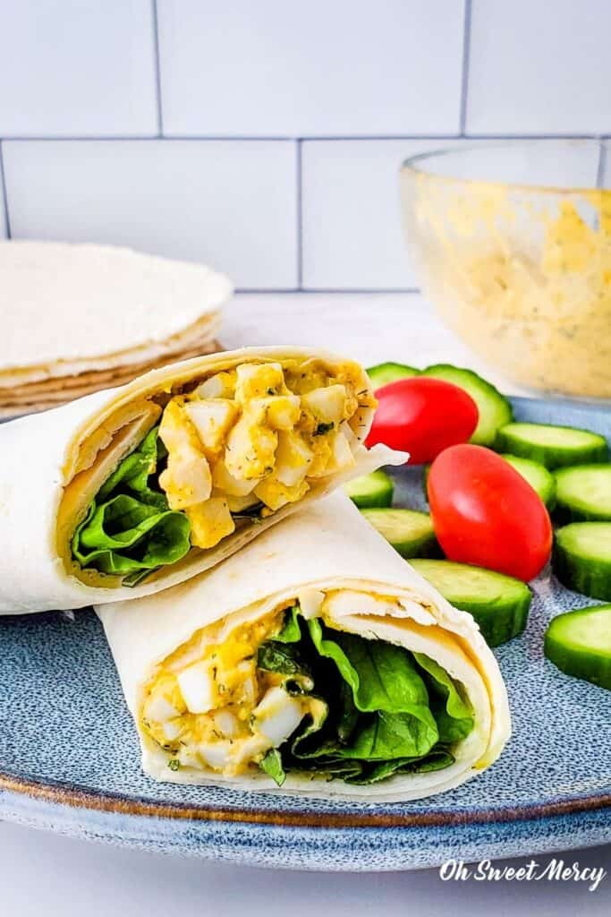 Creamy Ranch Egg Salad Wrap cut in half, on a plate with cucumber slices and cherry tomatoes.