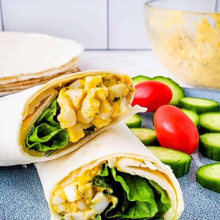 Creamy Ranch Egg Salad Wrap cut in half, on a plate with cucumber slices and cherry tomatoes.
