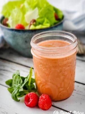 Small mason jar of raspberry basil vinaigrette with bowl of salad in background