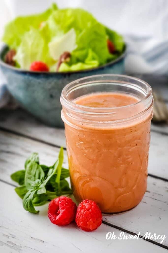 Small mason jar of raspberry basil vinaigrette with bowl of salad in background