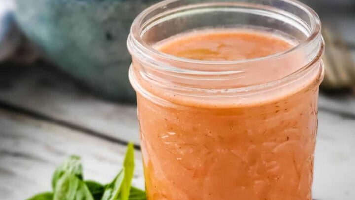 Small mason jar of raspberry basil vinaigrette with bowl of salad in background