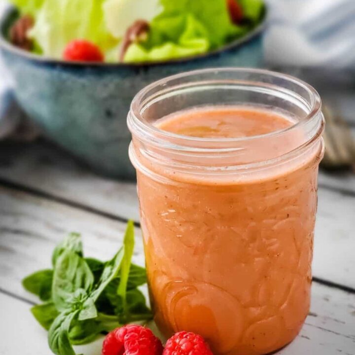 Small mason jar of raspberry basil vinaigrette with bowl of salad in background