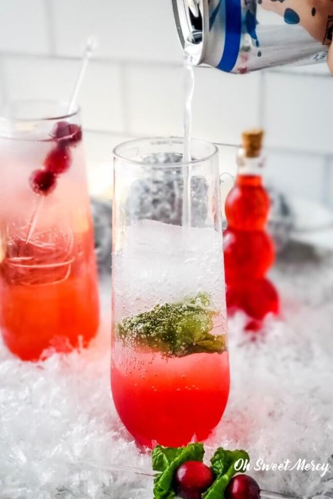 Pouring sparkling water into cranberry mocktail