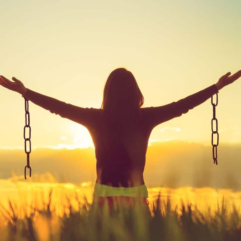 Woman in field with sun setting and broken chains hanging off her wrists