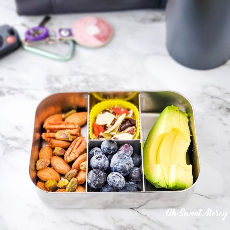 Vegan protein and healthy fats snack box - mixed nuts, unsweetened trail mix, blueberries, avocado slices.