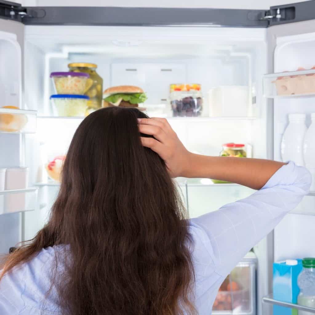 Confused woman looking in open refrigerator