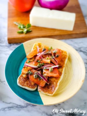 Plate of Mediterranean grilling cheese topped with fresh tomatoes, onions, herbs, and oil and vinegar