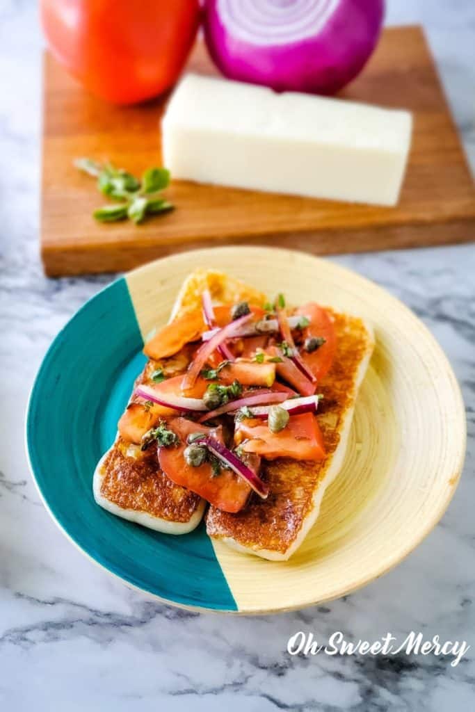 Plate of Mediterranean grilling cheese topped with fresh tomatoes, onions, herbs, and oil and vinegar