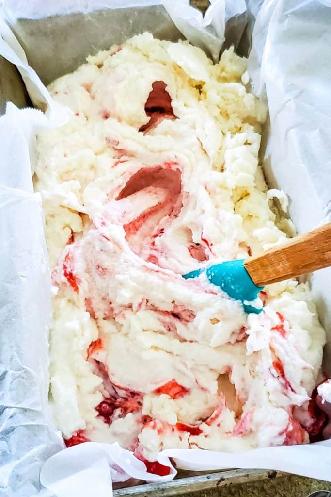 swirling strawberry rhubarb sauce into ice cream with a spatula