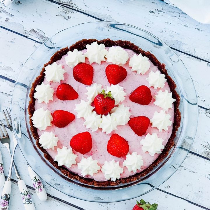 Whole low carb strawberry freezer pie decorated with dollops of whipped cream and strawberry halves