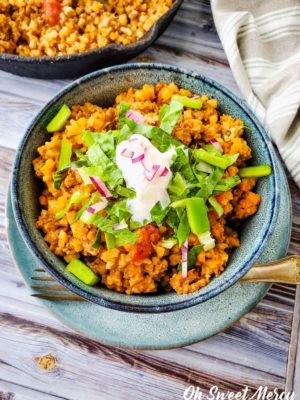 Bowl of low carb taco skillet made with cauli rice, topped with lettuce, sour cream, and onions