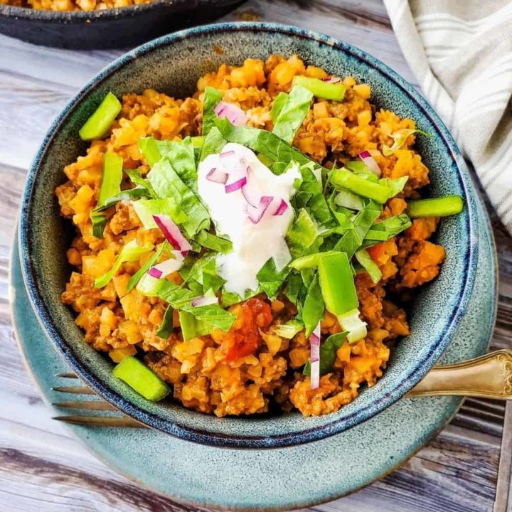 Bowl of low carb taco skillet made with cauli rice, topped with lettuce, sour cream, and onions