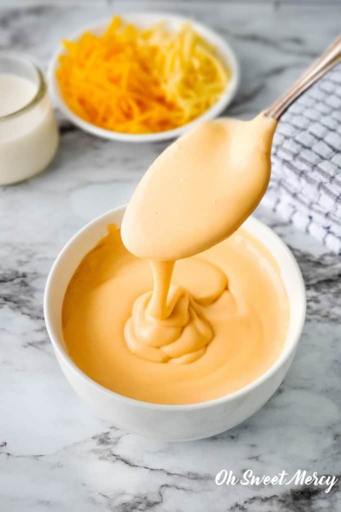 Spooning thick, creamy, easy low carb cheese sauce into a bowl.