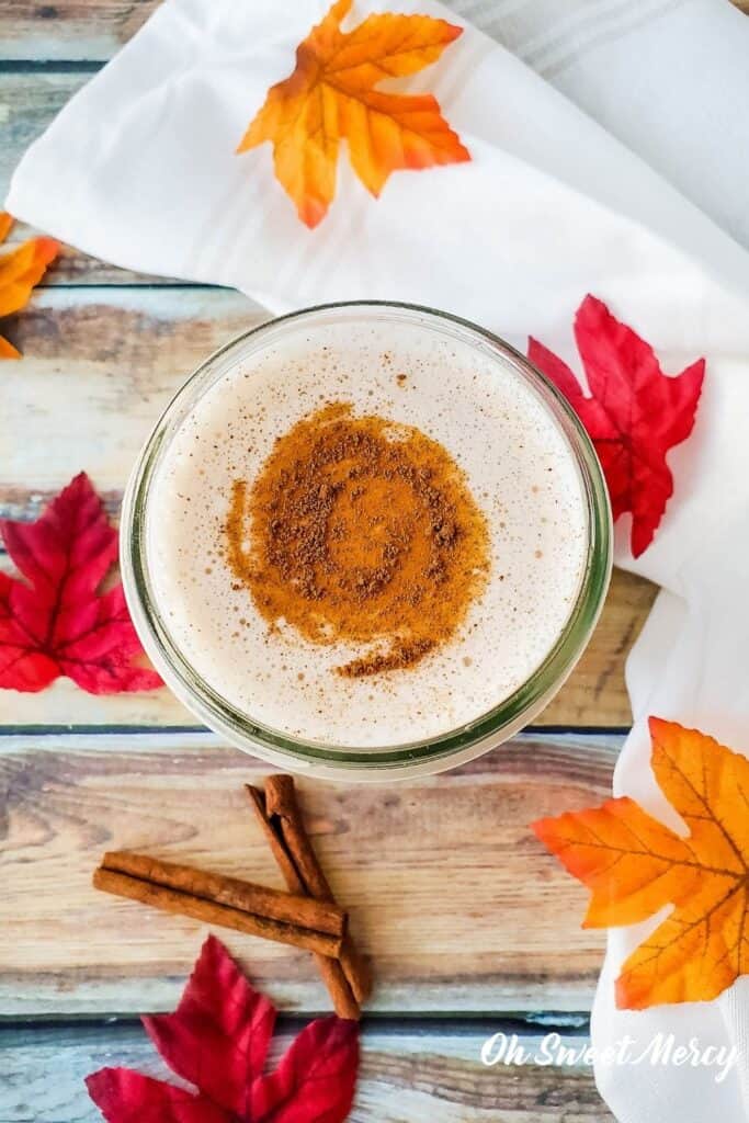 Overhead shot of shake in glass, surrounded by autumn colored maple leaves and cinnamon sticks