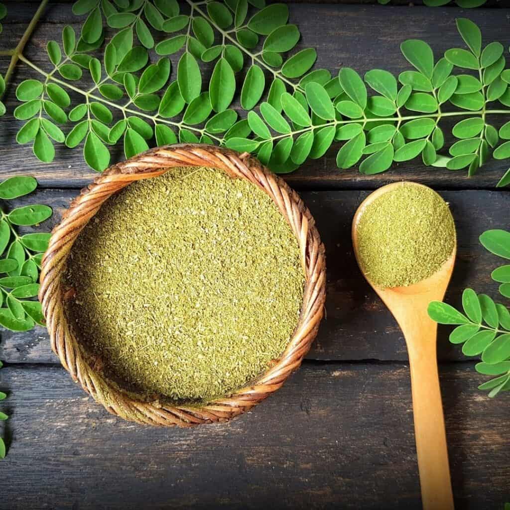 bowl of moringa with moringa leaves around it