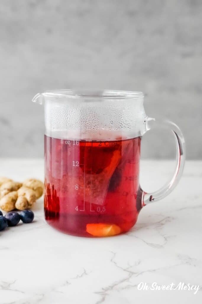 Brewing blueberry tea in a glass measuring cup, with ginger slices