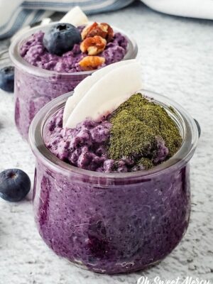 Small jar of dairy free coconut blueberry chia pudding topped with coconut flakes and greens powder