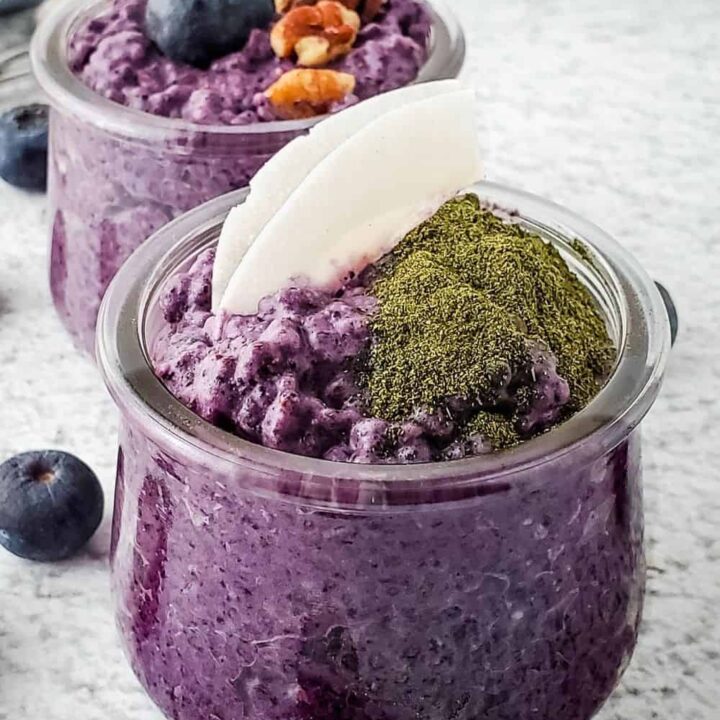 Small jar of dairy free coconut blueberry chia pudding topped with coconut flakes and greens powder