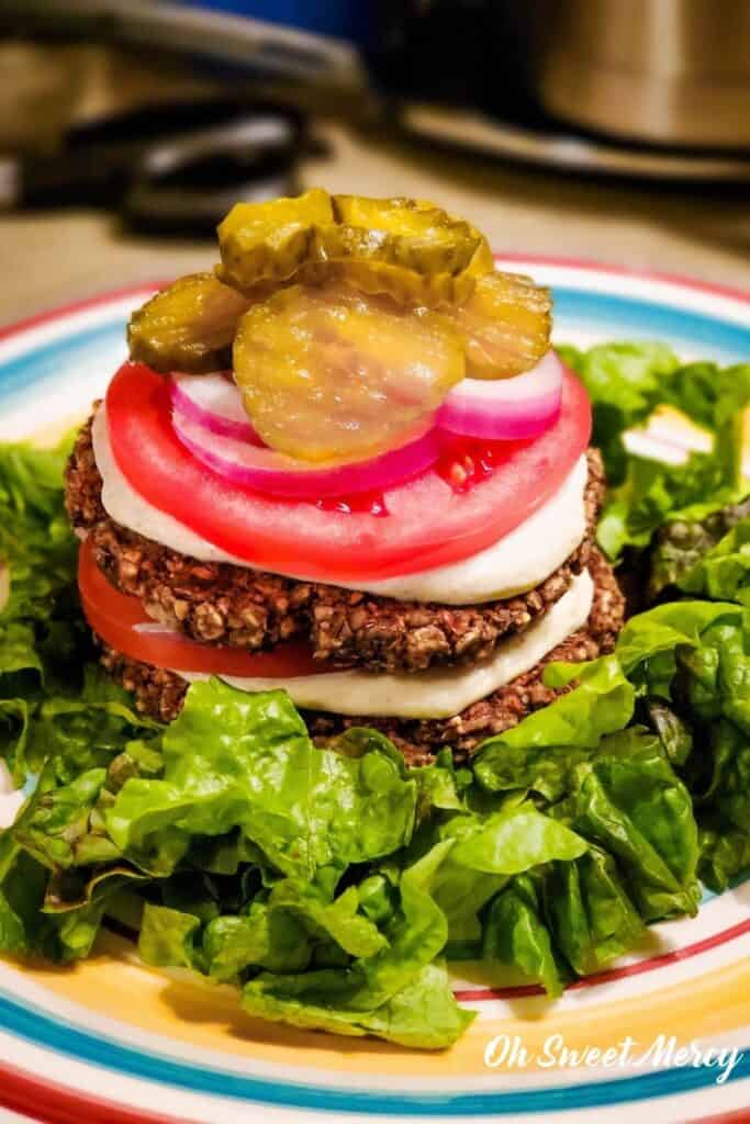 Lentil patties without a bun on a pile of lettuce and topped with low fat dijon sauce, tomato, onion, and pickles