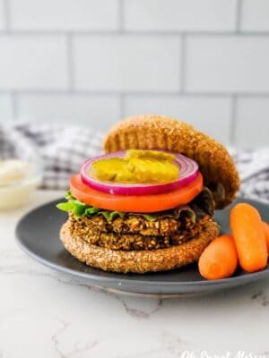 Low fat lentil burger on bun with lettuce, tomato, onion, and pickle on a plate with carrots