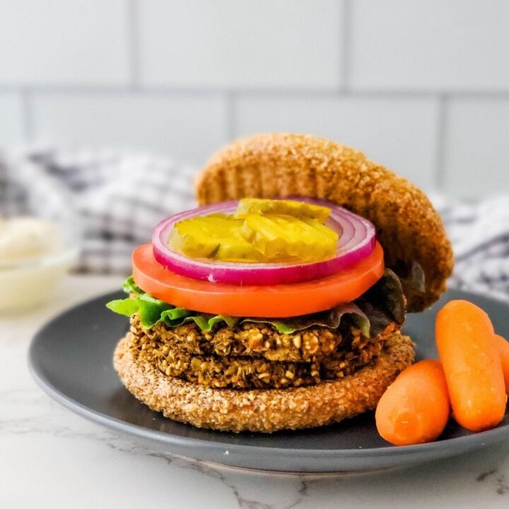 Low fat lentil burger on bun with lettuce, tomato, onion, and pickle on a plate with carrots