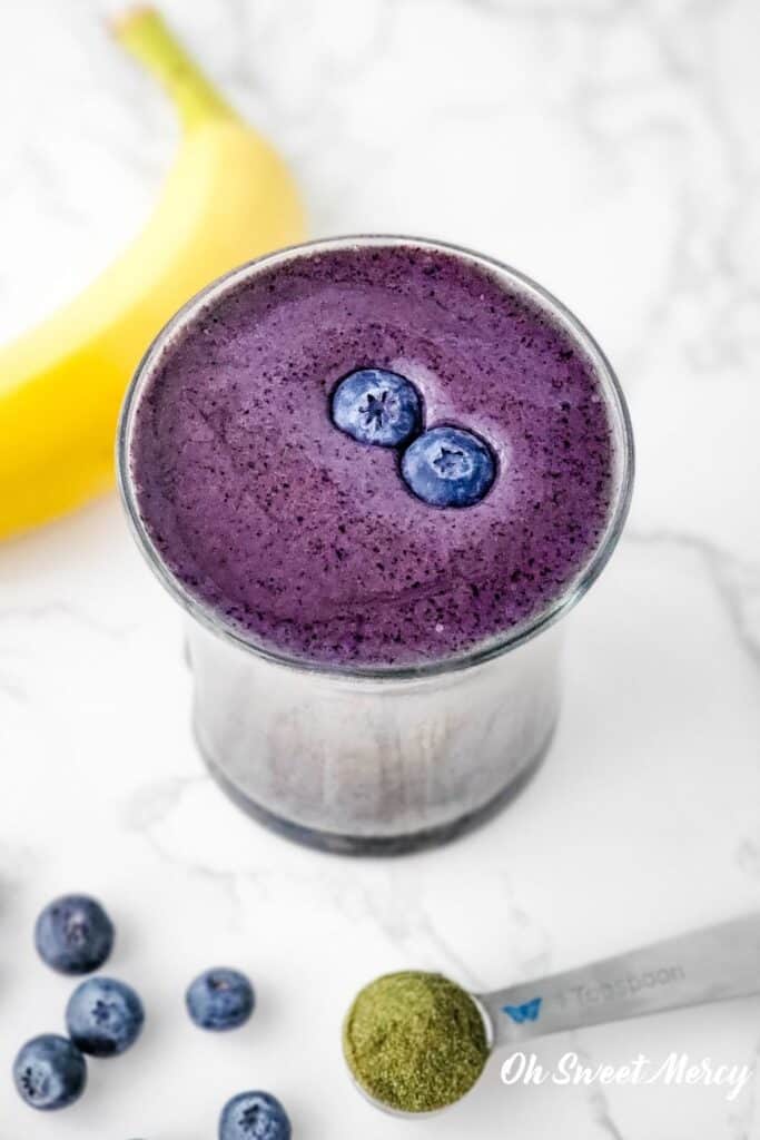 Overhead shot of glass of secret low fat blueberry smoothie with 2 fresh blueberries on top