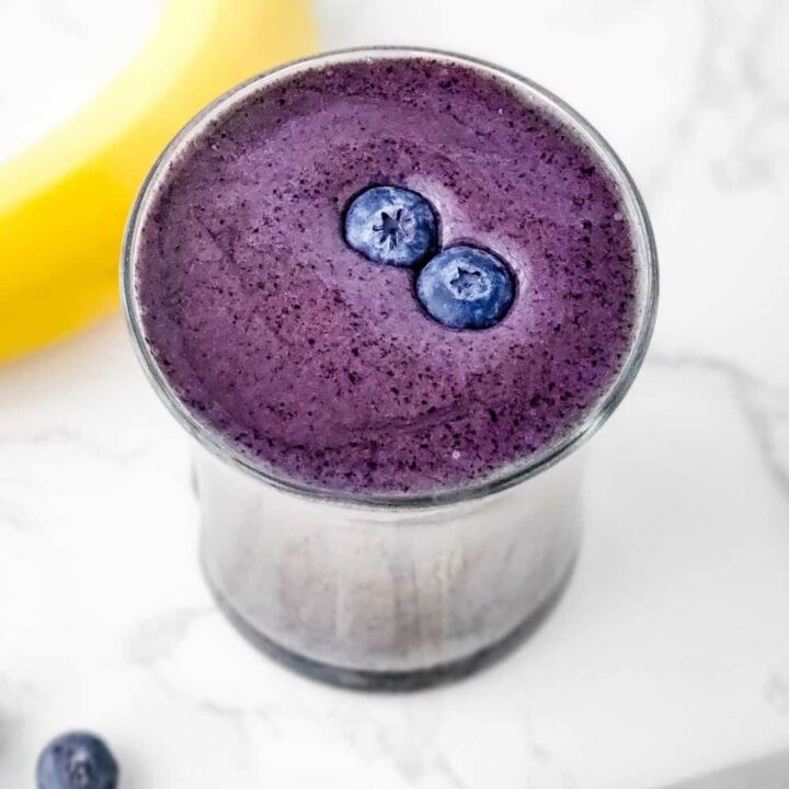 Overhead shot of glass of secret low fat blueberry smoothie with 2 fresh blueberries on top