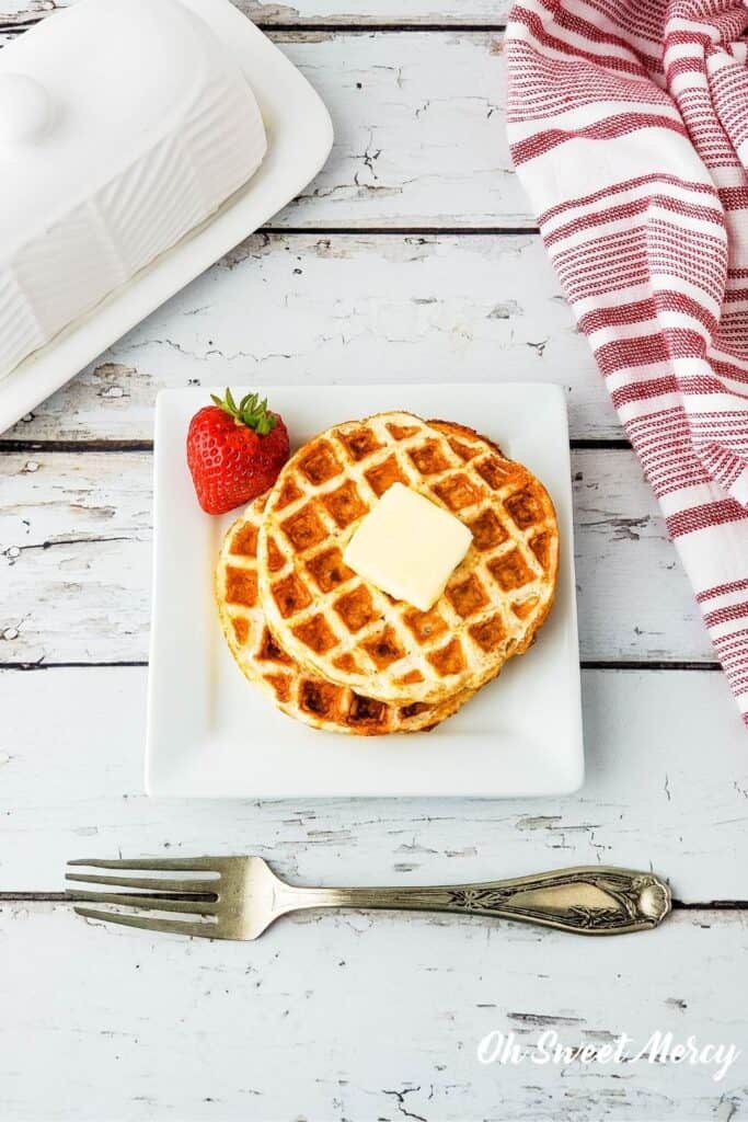 overhead shot of 2 waffles on a plate with a pat of butter and a strawberry on the side