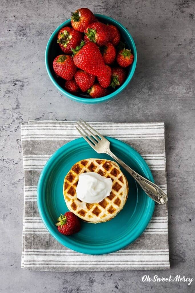 Overhead shot of waffles on aqua plate topped with yogurt, bowl of strawberries