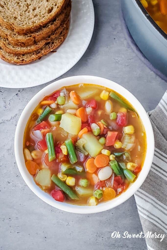 Bowl of homestyle vegetable soup with bread on a plate.