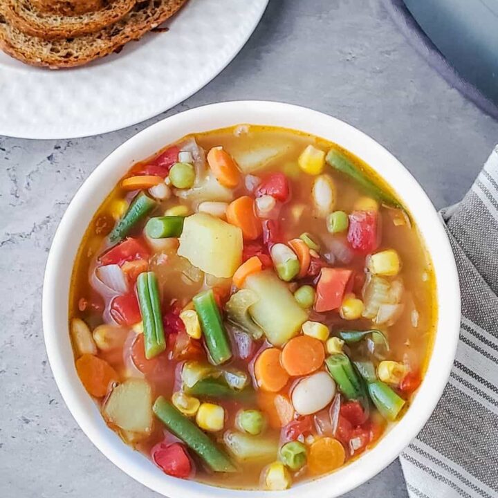Bowl of homestyle vegetable soup with bread on a plate.