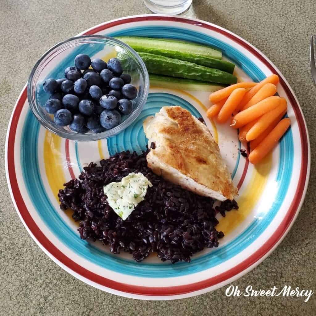 Plate of simple THM E meal example: black rice, chicken breast, carrots, cucumbers, blueberries.