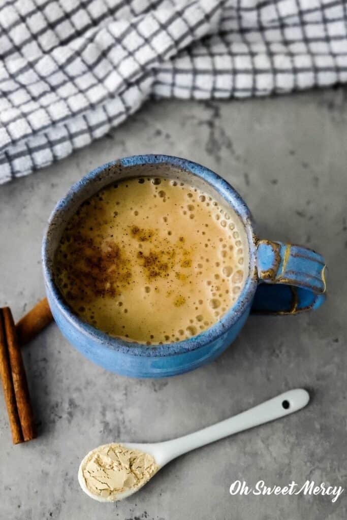 Overhead shot of blue mug containing moon milk with white ceramic spoon that has ashwagandha powder in front