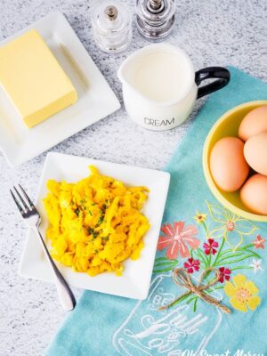 Plate of decadent scrambled eggs with ingredients around it and a pretty kitchen towel