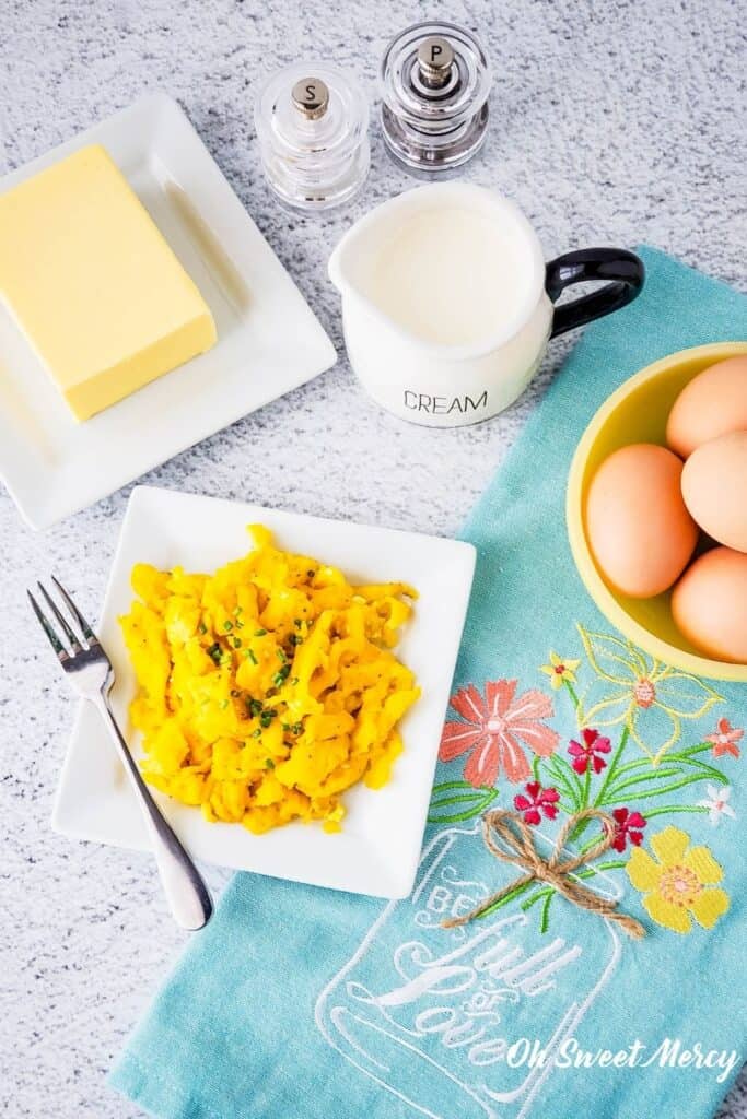 Plate of decadent scrambled eggs with ingredients around it and a pretty kitchen towel