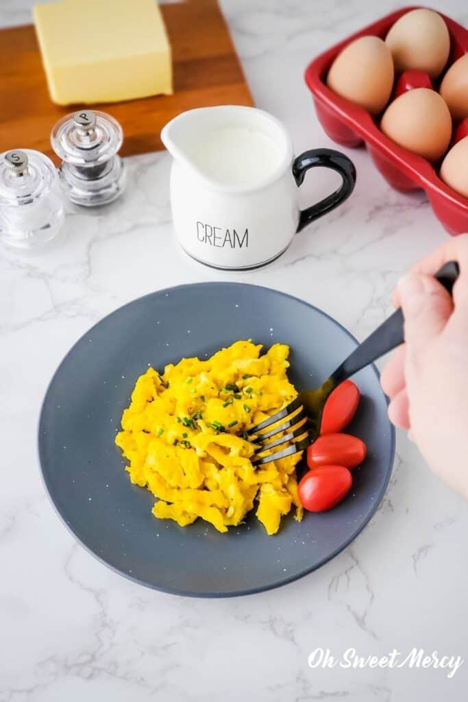 Eggs on plate and hand using fork to get a bite.