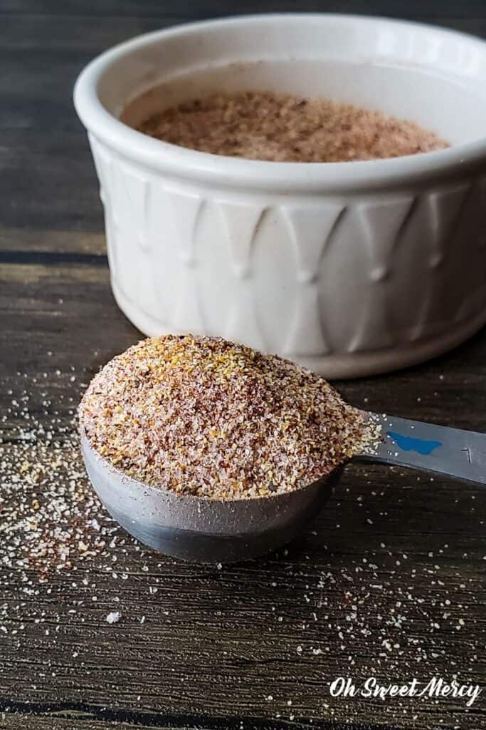 Heaping teaspoon of seasoning blend in front of white bowl.