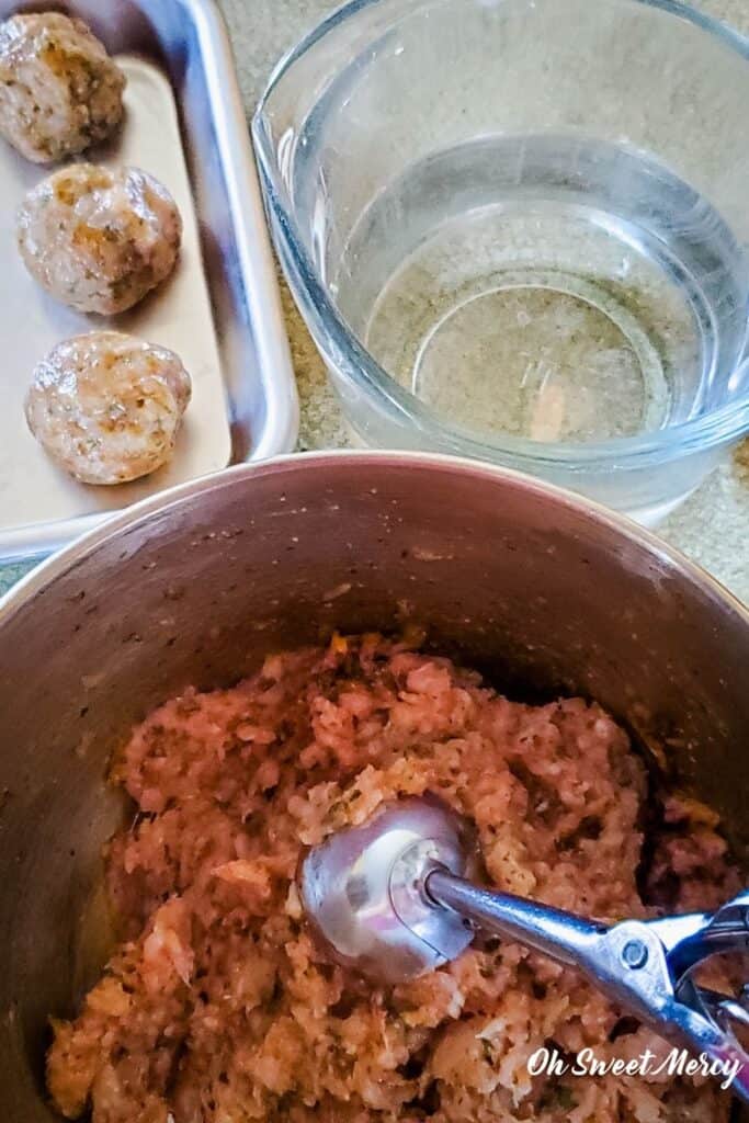 Mixing bowl with meatball mixture and cookie scoop, Pyrex glass measuring cup with water for less messy hands when making meatballs.