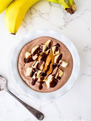 Overhead photo of white bowl with Chunky Monkey Yogurt Bowl drizzled with sugar free chocolate sauce