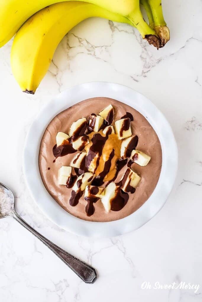 Overhead photo of white bowl with Chunky Monkey Yogurt Bowl drizzled with sugar free chocolate sauce