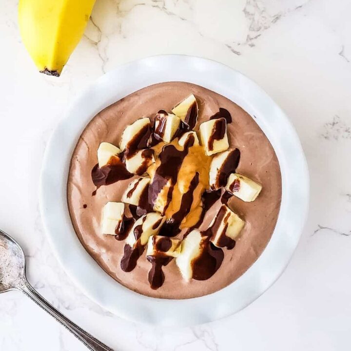 Overhead photo of white bowl with Chunky Monkey Yogurt Bowl drizzled with sugar free chocolate sauce