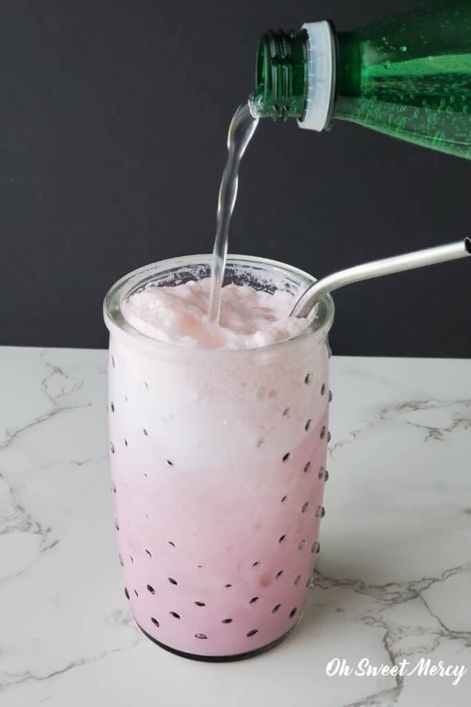 Pouring sparkling mineral water into glass with rest of ingredients