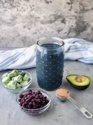 Glass of my Chocolate Blueberry Smoothie (AKA The Breakfast Smoothie) with some ingredients that are in it: blueberries, okra, cacao powder, avocado