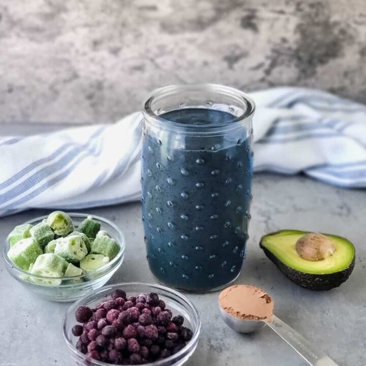 Glass of my Chocolate Blueberry Smoothie (AKA The Breakfast Smoothie) with some ingredients that are in it: blueberries, okra, cacao powder, avocado