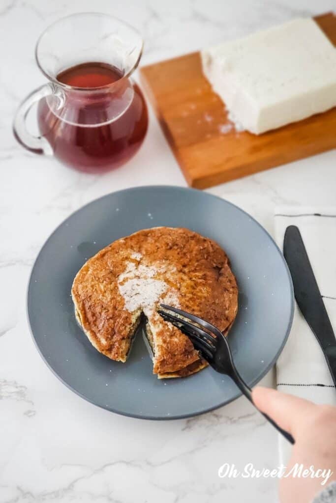 Millet pancake with vegan butter and sugar free syrup on a plate, fork cutting into pancakes