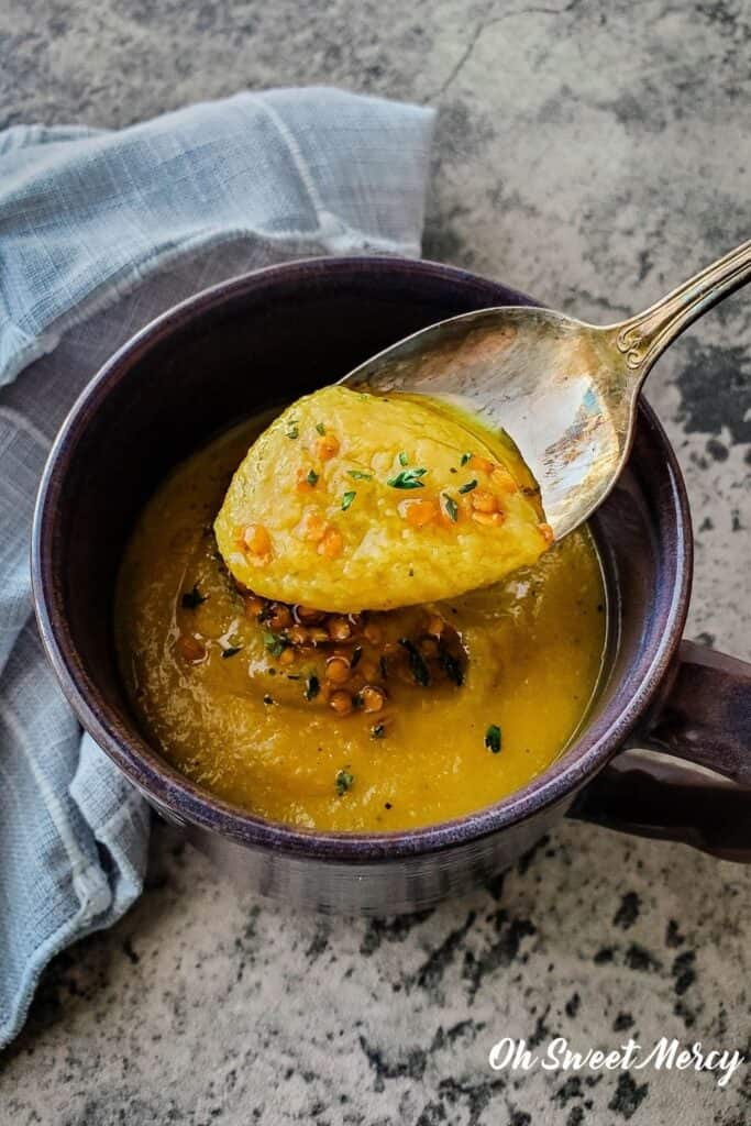 Spoonful of thick, creamy Red Lentil and Delicata Squash Soup over a mug of soup.