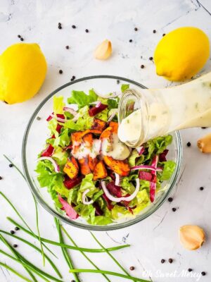 Pouring Creamy Lemon Garlic Salad Dressing over a bowl of salad