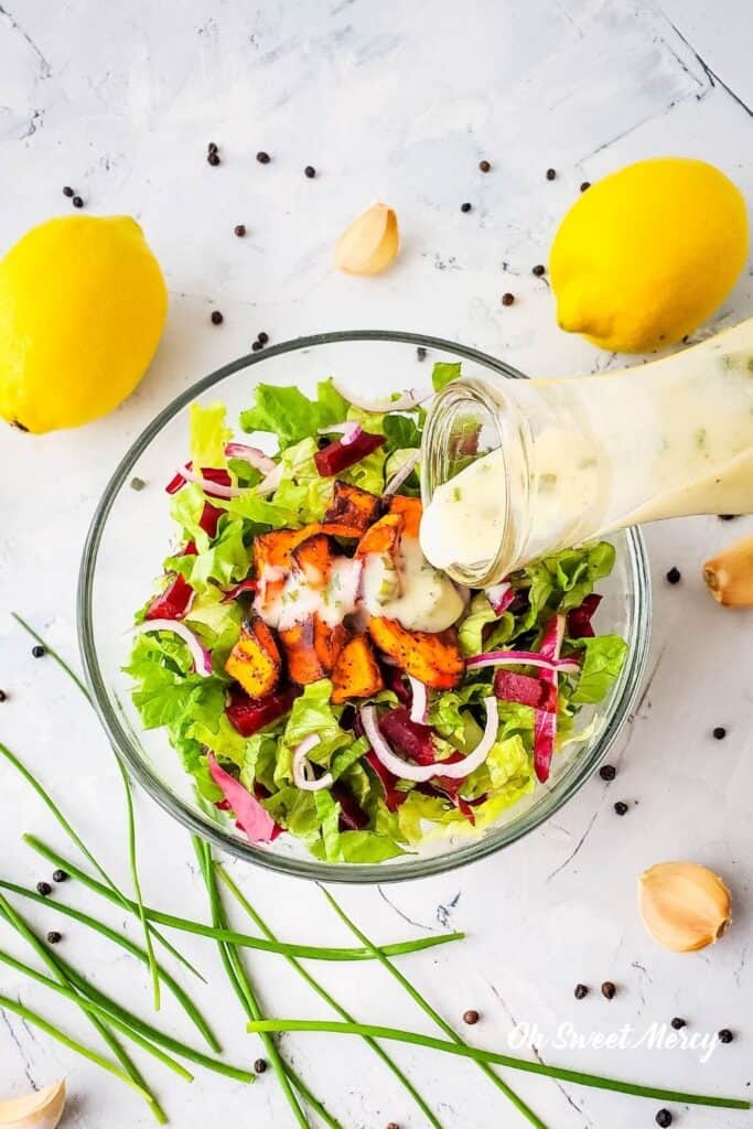 Pouring Creamy Lemon Garlic Salad Dressing over a bowl of salad